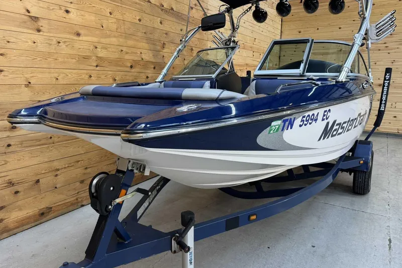 Slide: The Image of 2011 MasterCraft X2 boat on trailer, blue and white, wooden background. - 3