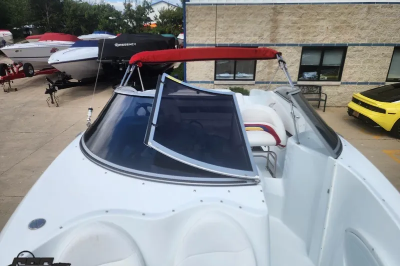 Slide: The Image of 2005 Baja 242 Islander boat with red canopy, parked near other boats and a yellow car. - 48