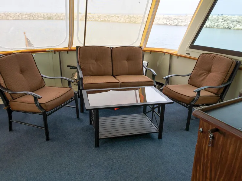 Slide: The Image of 1985 Hatteras 56 Motor Yacht interior with brown seating and glass table, overlooking water. - 7