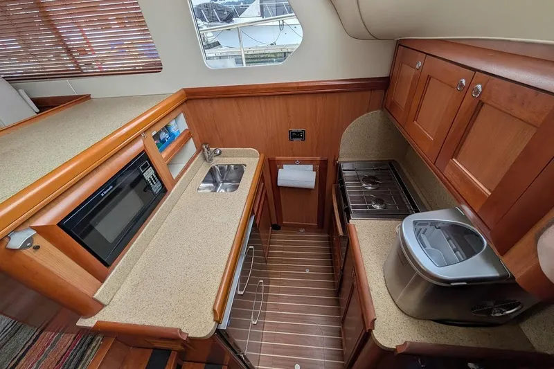 Slide: The Image of 2008 Mainship 38 yacht kitchen with wood cabinets, microwave, sink, and stove. - 19