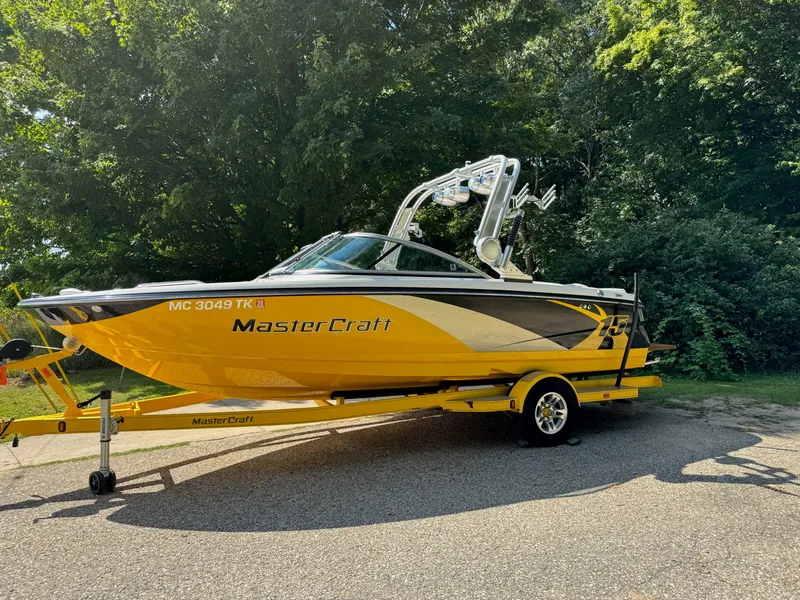 Slide: The Image of 2012 MasterCraft X-15 boat in vibrant yellow on a trailer, parked near lush greenery. - 1