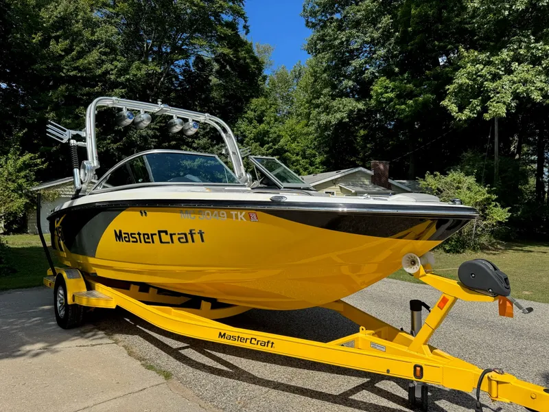 Slide: The Image of 2012 MasterCraft X-15 boat on yellow trailer, parked outdoors with trees in background. - 4