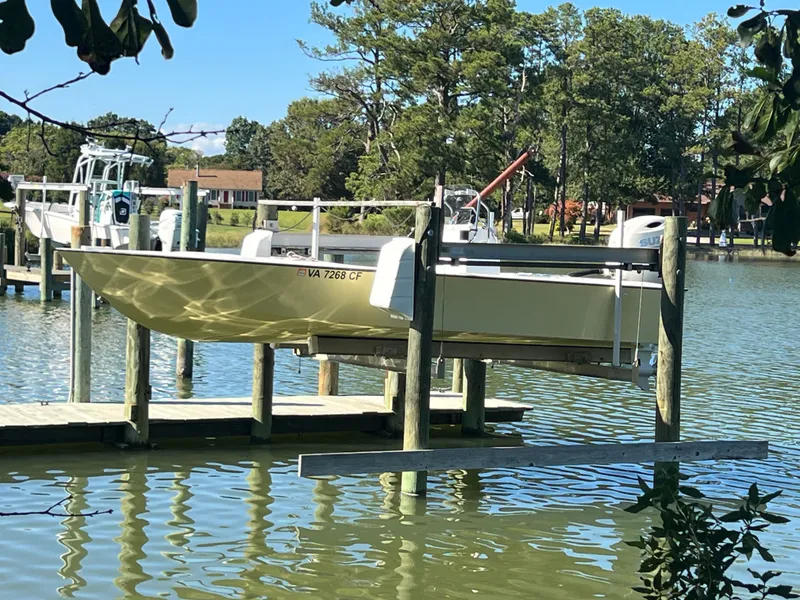 The Image of Custom 24 boat on lift at dock, surrounded by trees and calm water, 2022 model. - 0