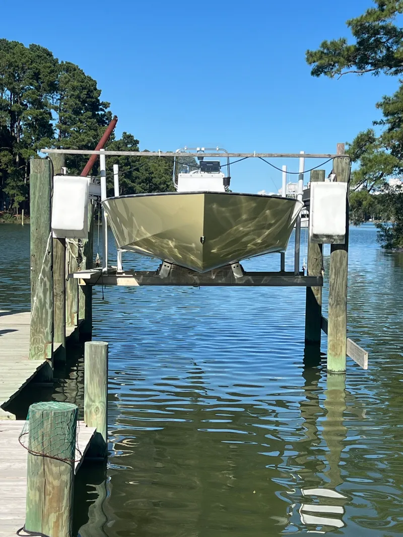 Slide: The Image of Custom 24 boat on lift, docked by serene lake, surrounded by trees, 2022 model. - 2