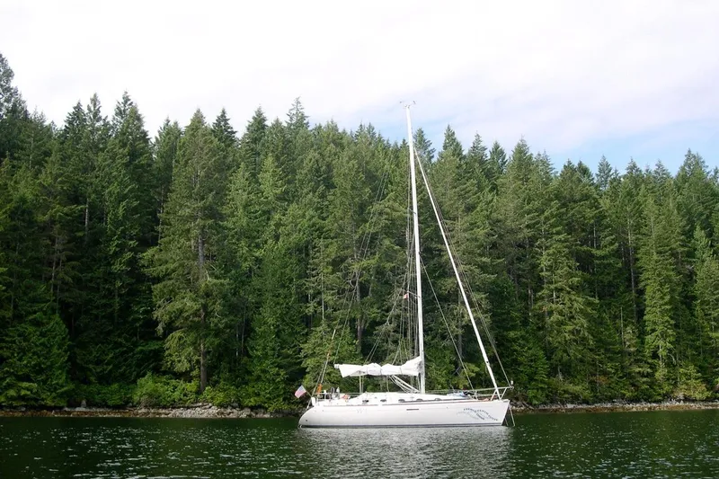 Slide: The Image of Sailboat Beneteau First 35s-7 (1994) on calm water, surrounded by lush green forest. - 5