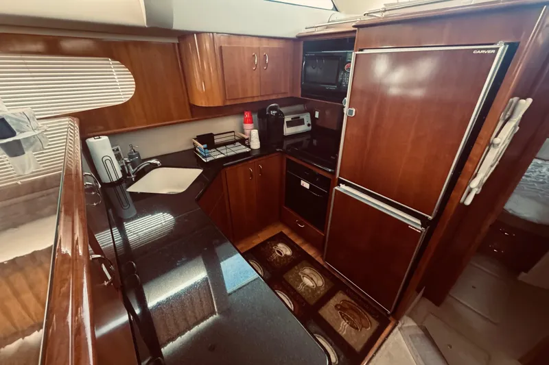 Slide: The Image of 2005 Carver 466 Motor Yacht kitchen with wooden cabinetry, appliances, and black countertops. - 21