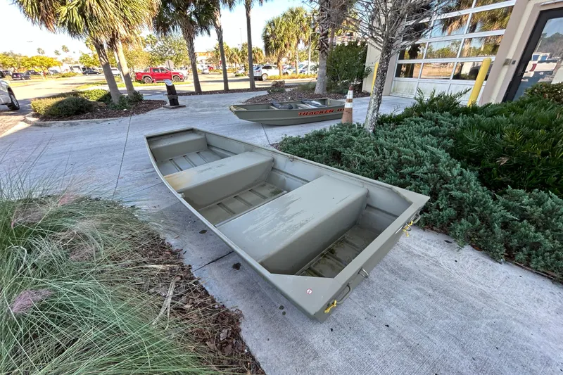 Slide: The Image of 2026 Tracker Grizzly 12 Jon boat on concrete near greenery and palm trees. - 2