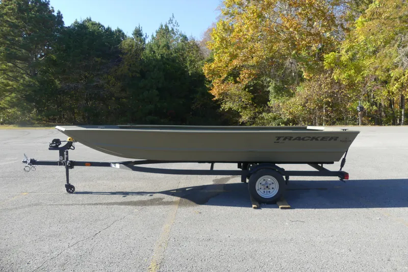 Slide: The Image of 2026 Tracker Grizzly 1648 Utility boat on trailer in a parking lot, surrounded by trees. - 2
