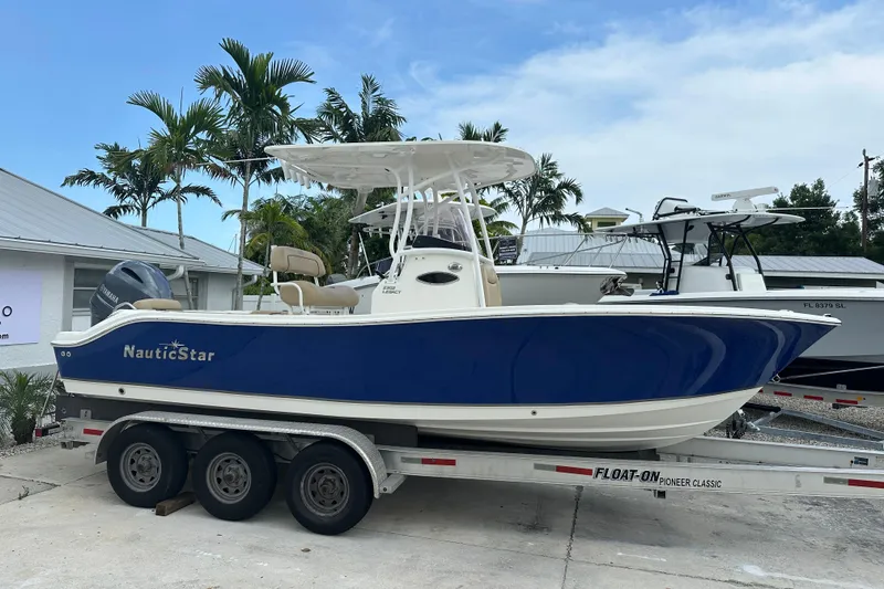 Slide: The Image of 2019 NauticStar 2302 Legacy boat on trailer, blue hull, palm trees in background. - 8