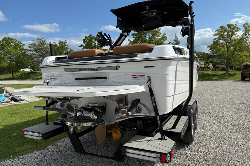 Slide: The Image of 2026 Centurion Ri245 boat on trailer, rear view, parked on gravel with trees in background. - 5