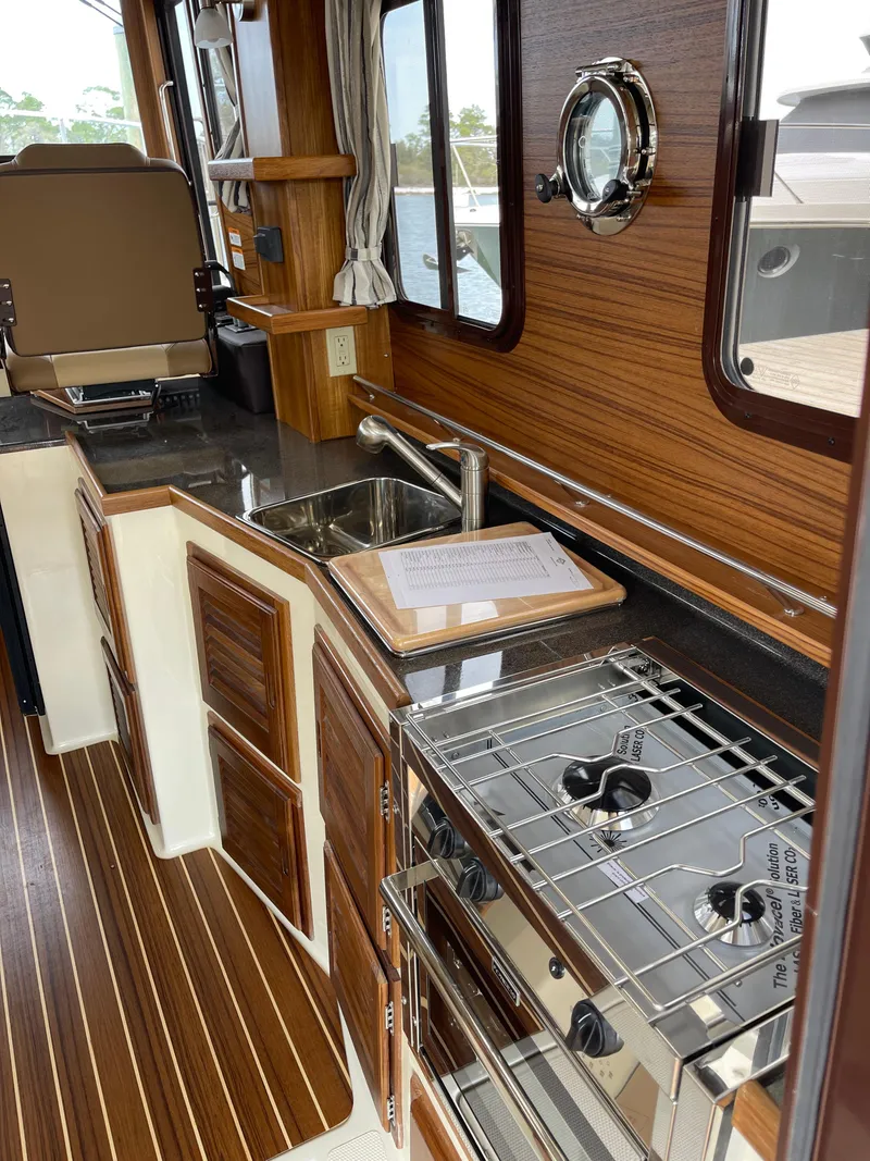 Slide: The Image of 2023 Ranger Tugs R-31 CB kitchen with stove, sink, and wooden cabinetry. - 16