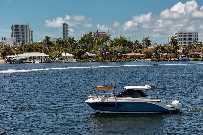 Slide: The Image of 2022 Sea Ray Sundancer 320 Outboard cruising on a sunny day with city skyline backdrop. - 4