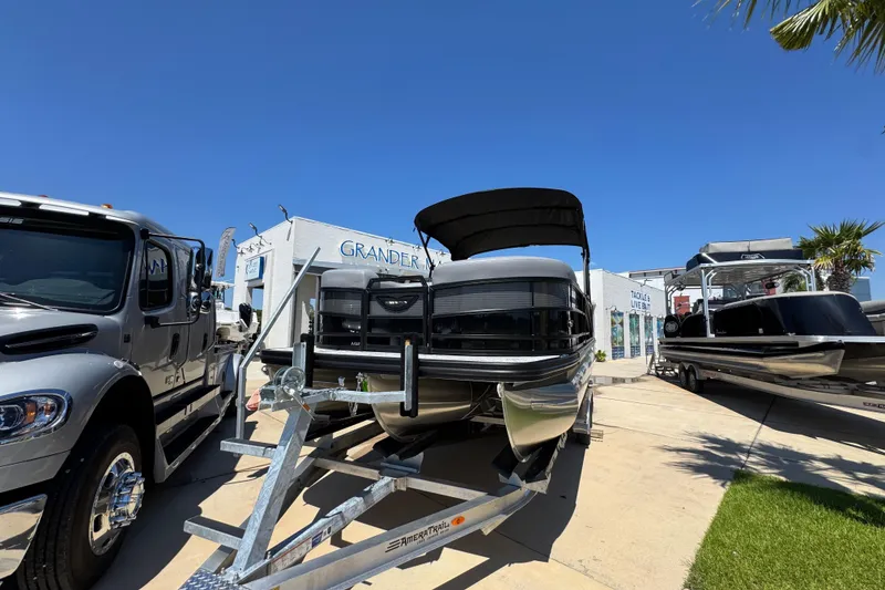 Slide: The Image of 2026 Bennington 22 MFB pontoon boat on trailer, parked beside a truck under clear blue sky. - 4