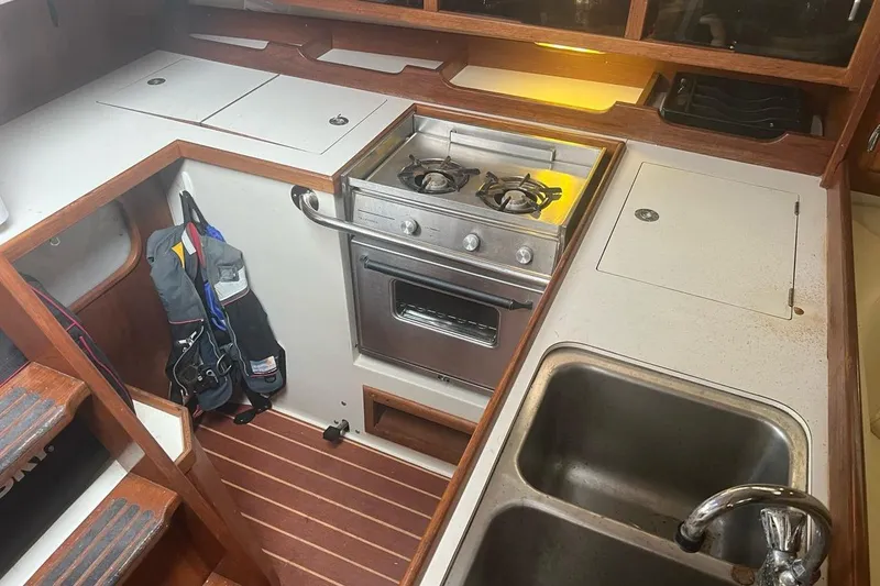 Slide: The Image of Interior of a 1992 Catalina Sloop showing a compact kitchen with stove and sink. - 8