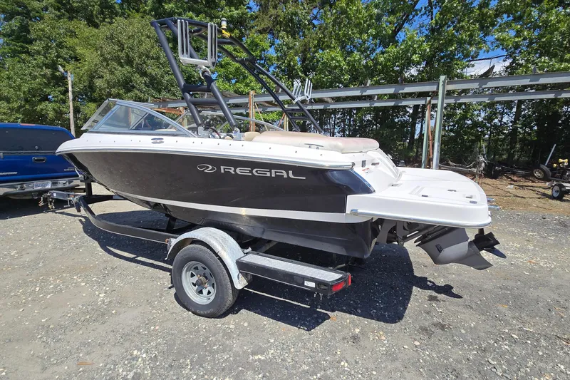 The Image of 2015 Regal 1900 Bowrider boat on trailer, parked outdoors, surrounded by trees. - 0