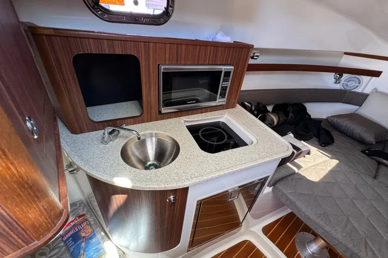Slide: The Image of 2015 Pursuit OS 285 Offshore cabin with kitchenette, featuring sink, microwave, and stove. - 27