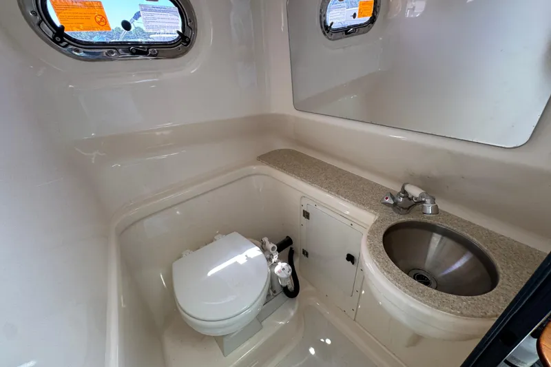 Slide: The Image of 2015 Pursuit OS 285 Offshore boat bathroom with toilet, sink, and porthole windows. - 30