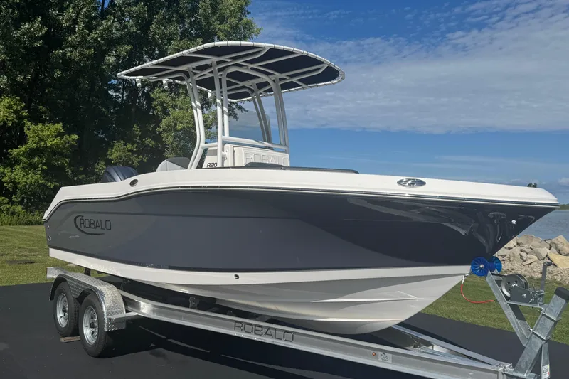 Slide: The Image of 2026 Robalo R202 Explorer boat on trailer, parked outdoors with trees and sky background. - 2