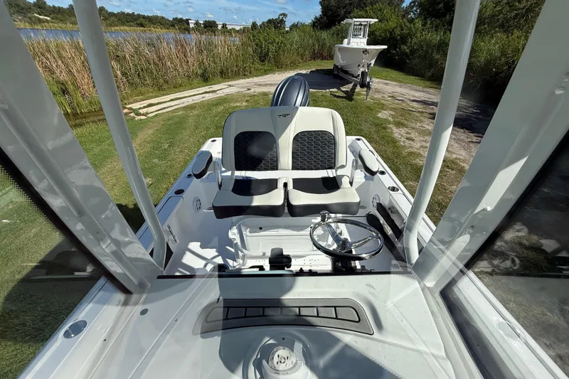 Slide: The Image of 2026 Tidewater 2210 Carolina Bay boat interior with steering wheel and seating, near grassy shoreline. - 22