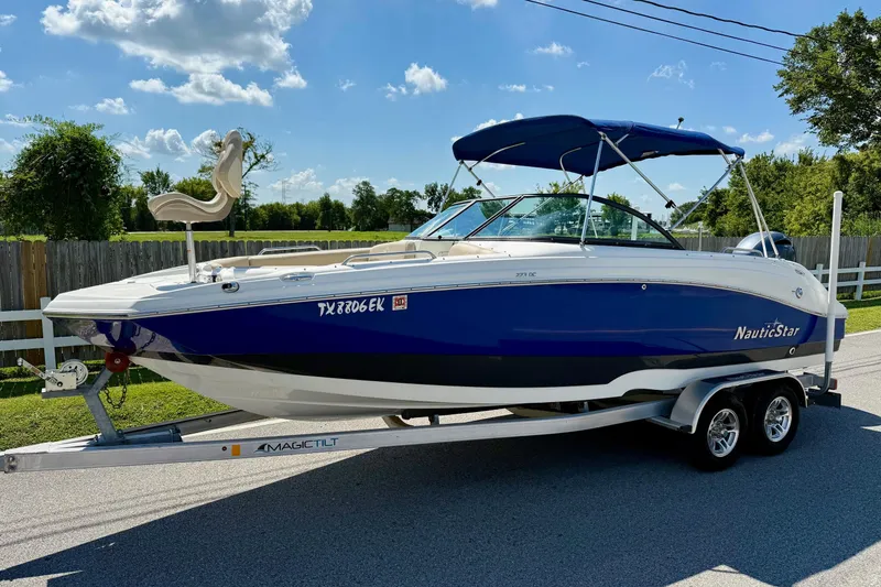 The Image of 2018 NauticStar 223 DC boat on trailer, blue and white, parked on road. - 1