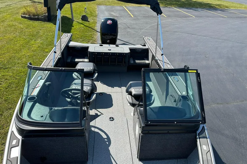 Slide: The Image of 2026 Lund 1875 Fisherman boat interior with seating and windshield, parked on pavement. - 15