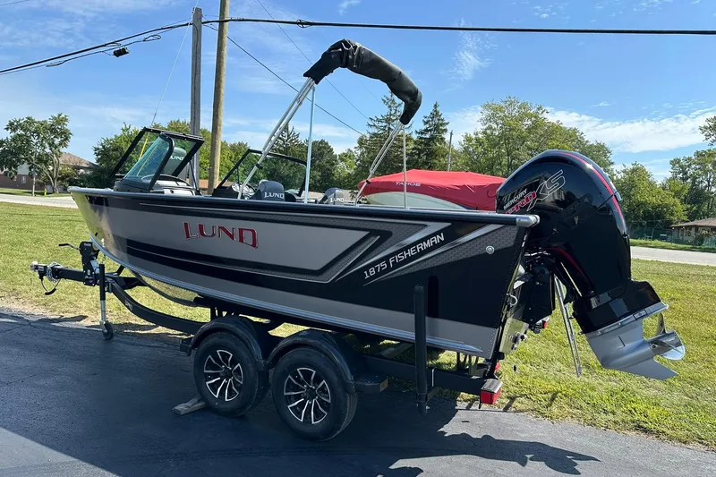Slide: The Image of 2026 Lund 1875 Fisherman boat on trailer, parked outdoors, featuring a powerful outboard motor. - 5
