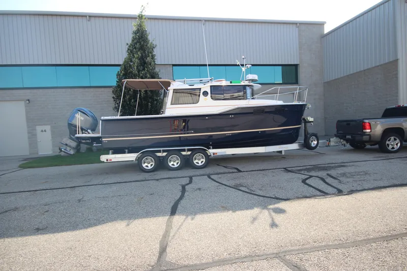 The Image of 2026 Ranger Tugs R-27 boat on trailer outside industrial building. - 0