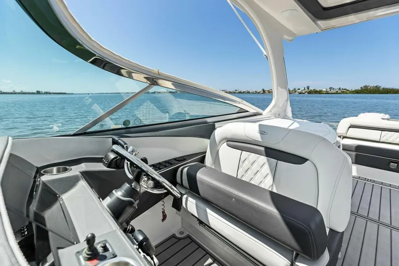 Slide: The Image of 2022 Regal 33 OBX boat interior with luxurious seating and steering, overlooking serene waters. - 19