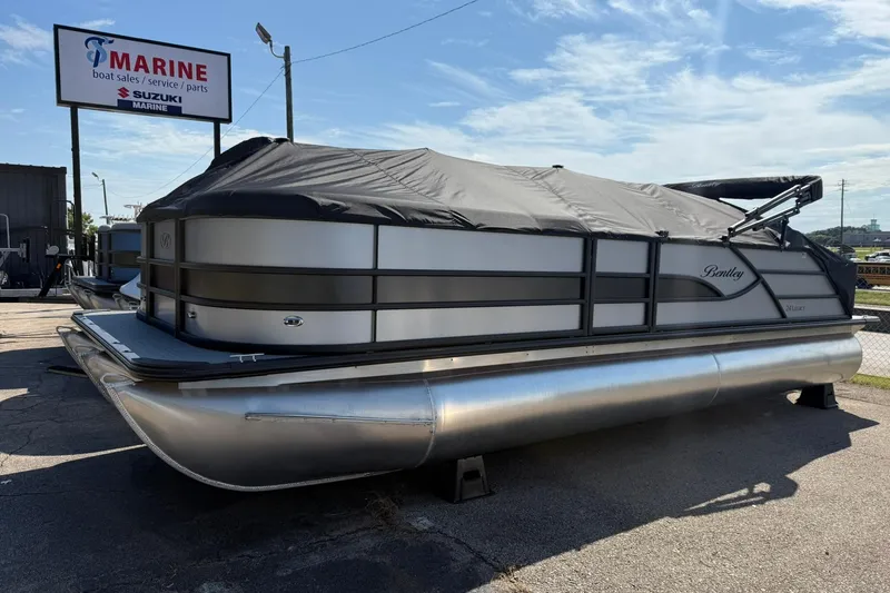 Slide: The Image of 2025 Bentley Pontoons Legacy 243 QSB covered, parked at a marine dealership under a clear sky. - 20