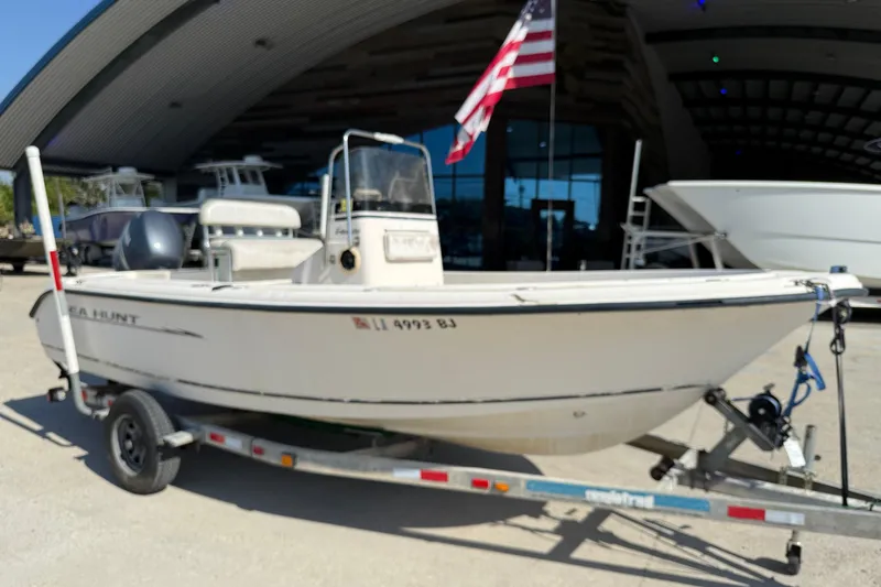 Slide: The Image of 2004 Sea Hunt Triton 186 boat on trailer with American flag, parked outside a building. - 2
