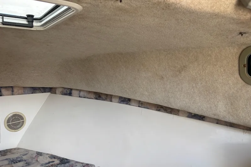 Slide: The Image of Interior cabin of 2000 Shamrock 260 Express boat, featuring beige upholstery and a small window. - 24