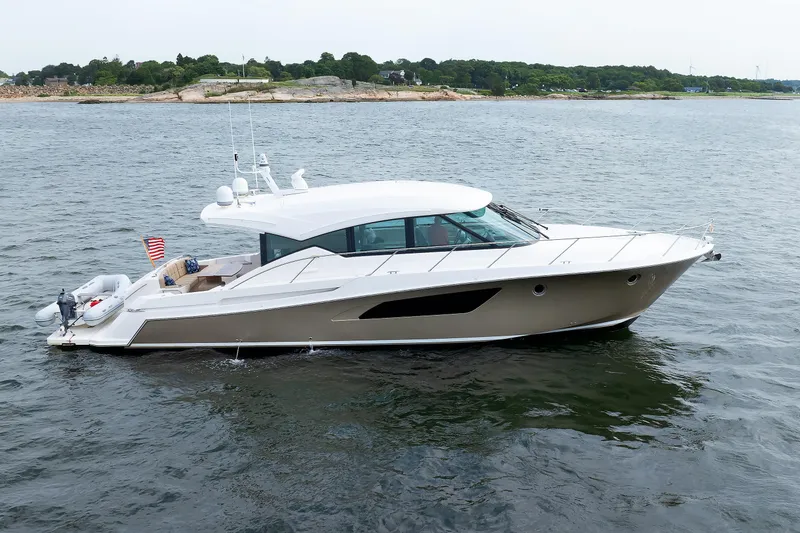 The Image of 2014 Tiara 5000 Coupe yacht cruising on calm waters near a rocky shoreline. - 0