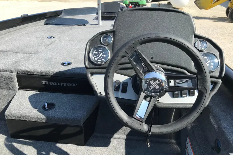 Slide: The Image of 2026 Ranger RT188P boat interior with steering wheel and seats, parked near a warehouse. - 7