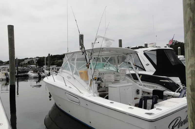 Slide: The Image of 2002 Rampage 30 Open boat docked at marina, featuring fishing rods and spacious deck. - 6