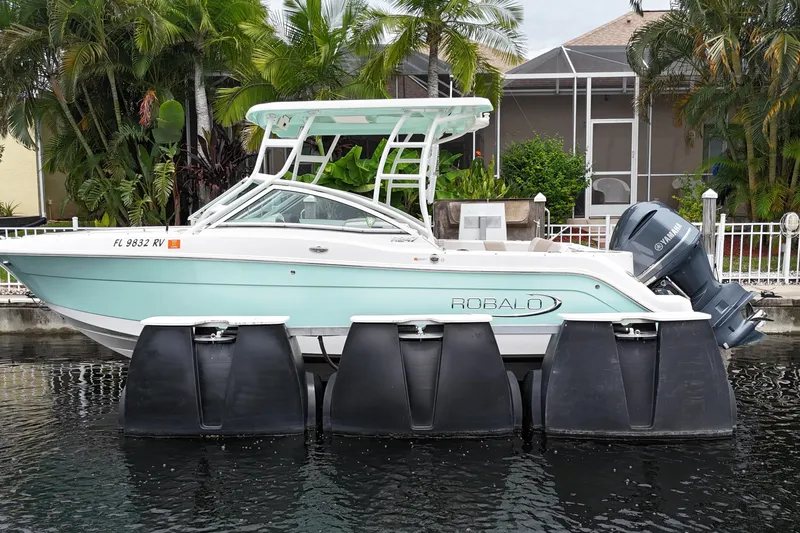 Slide: The Image of 2019 Robalo R247 Dual Console boat docked on water, surrounded by lush greenery. - 3