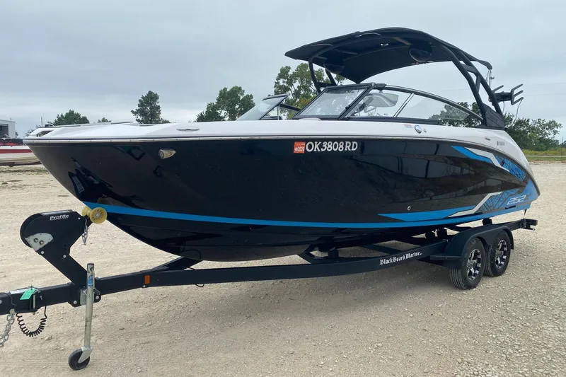 Slide: The Image of 2021 Yamaha Boats 252XE on trailer, sleek black and blue design, parked outdoors. - 2