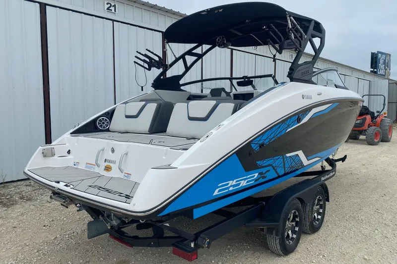 Slide: The Image of 2021 Yamaha Boats 252XE on trailer, white and blue design, parked near storage units. - 5