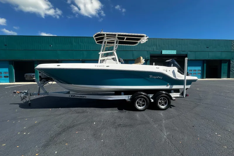 The Image of 2022 Trophy T22 boat on trailer, parked outside a teal building under a clear blue sky. - 1