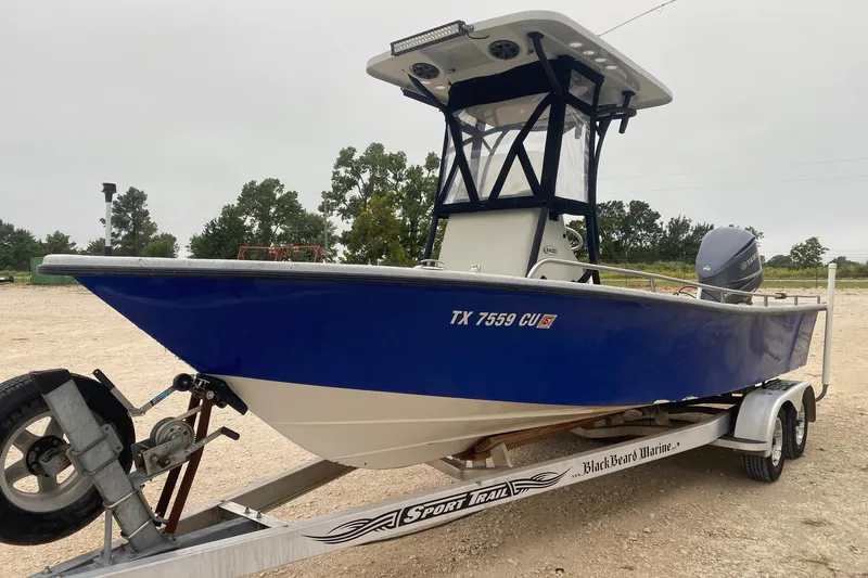 Slide: The Image of 2015 Blazer Bay 2400 boat on trailer, blue hull, parked outdoors. - 2