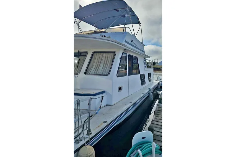 Slide: The Image of 1996 Gibson 41 Classic Houseboat docked, featuring a blue canopy and white exterior. - 4