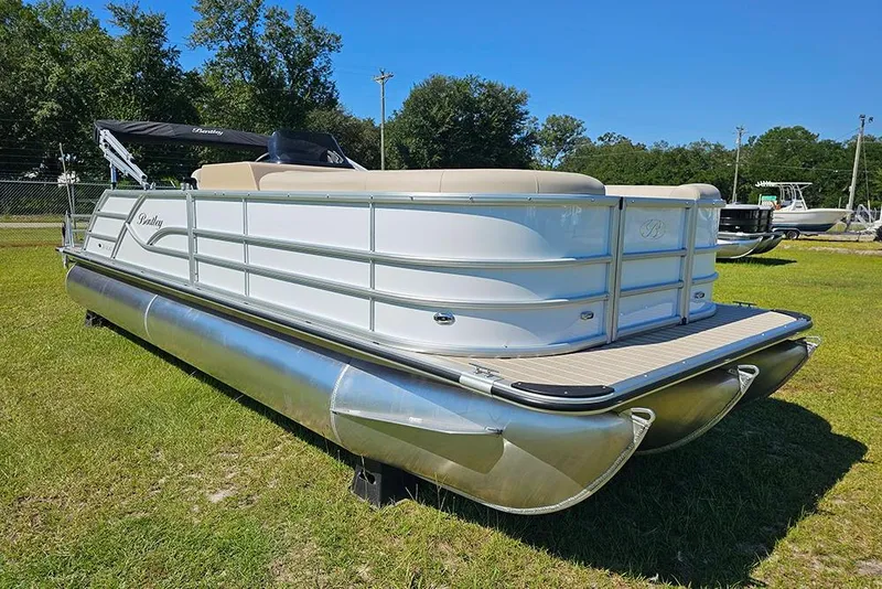 Slide: The Image of 2026 Bentley Pontoons 243 Legacy Swingback with Suzuki outboard motor, parked outdoors. - 2