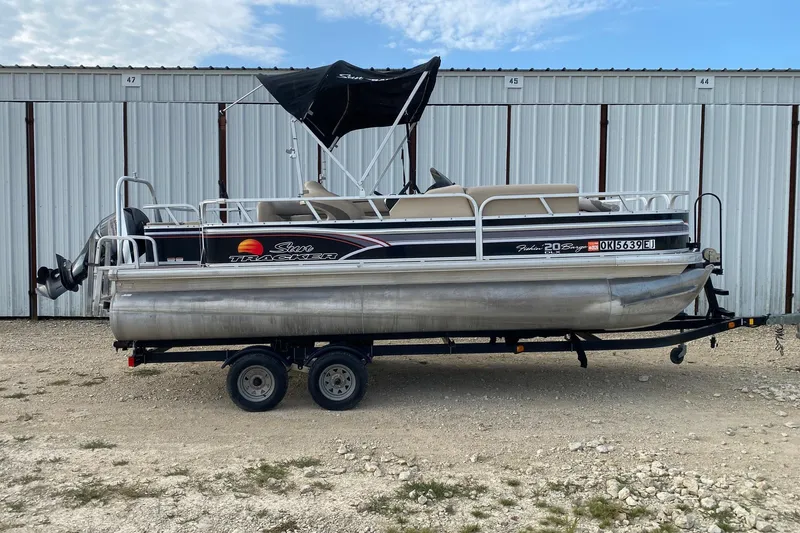 The Image of 2015 Sun Tracker Fishin' Barge 20 DLX pontoon boat on trailer, parked by storage units. - 0