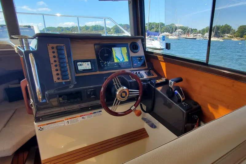 Slide: The Image of 2024 Ranger Tugs R-27 helm with navigation screens and steering wheel, overlooking marina. - 16