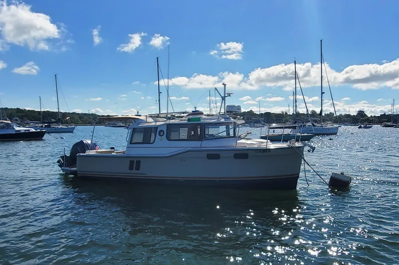 Slide: The Image of 2024 Ranger Tugs R-27 boat anchored in a sunny harbor with other vessels. - 5