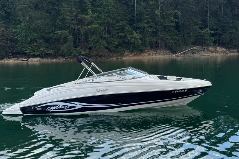 The Image of 2005 Rinker 232 Captiva Bowrider on serene lake with forested shoreline. - 0