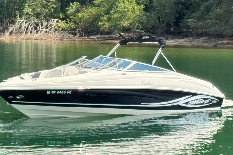 Slide: The Image of 2005 Rinker 232 Captiva Bowrider on calm water, surrounded by lush greenery. - 15