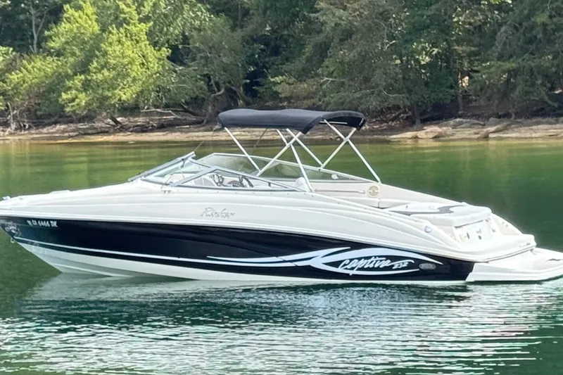 Slide: The Image of 2005 Rinker 232 Captiva Bowrider on calm lake with lush green forest backdrop. - 18
