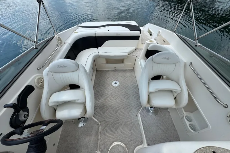 Slide: The Image of 2005 Rinker 232 Captiva Bowrider interior with white seating and steering wheel, on calm water. - 19