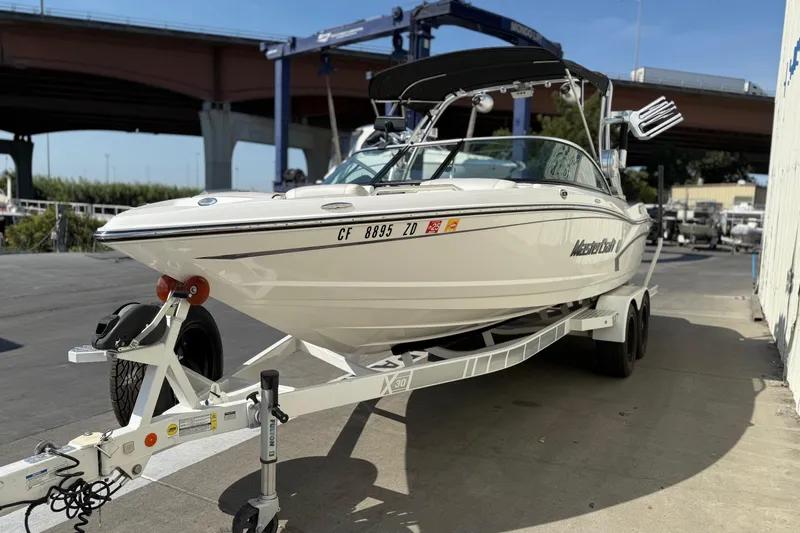 Slide: The Image of 2015 MasterCraft X30 boat on trailer, parked outdoors under a bridge. - 2