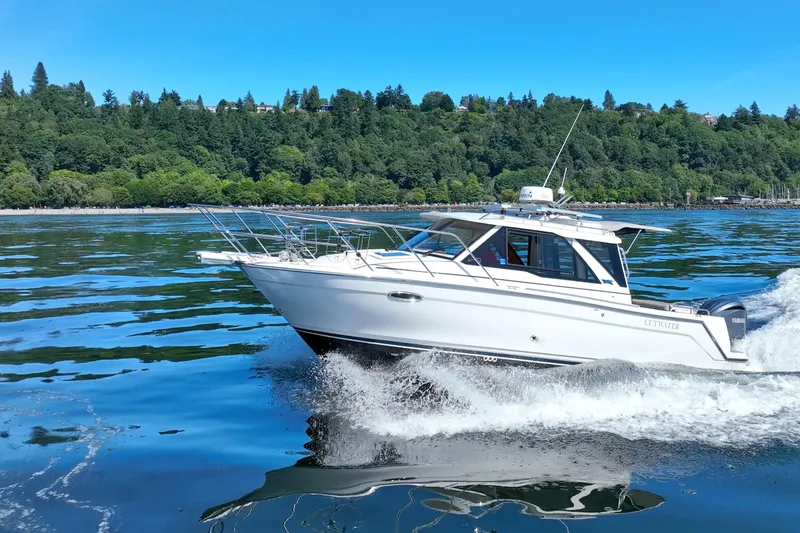 Slide: The Image of 2024 Cutwater C-248 Coupe cruising on a scenic lake with lush green shoreline. - 5